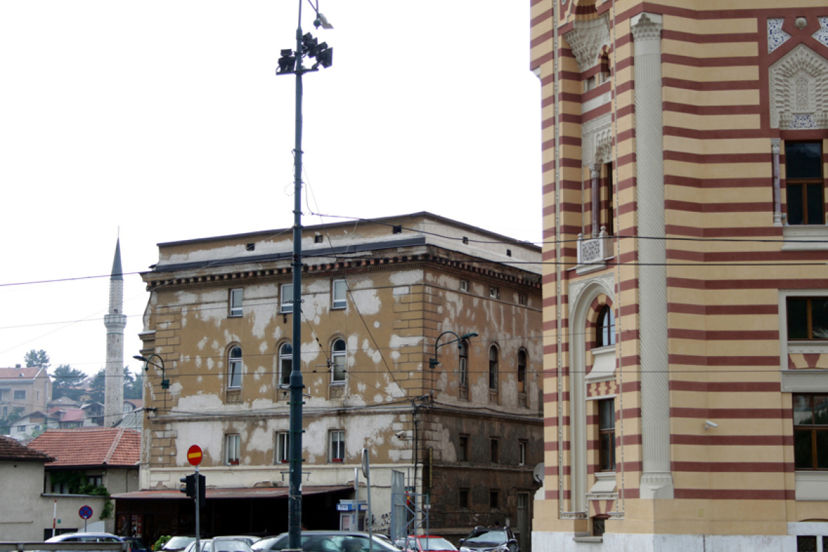 Neben der frisch renovierten Vijećnica verwittert ein Wohngebäude vor sich hin. Im Hintergrund das Minarett einer frisch renovierten Moschee.