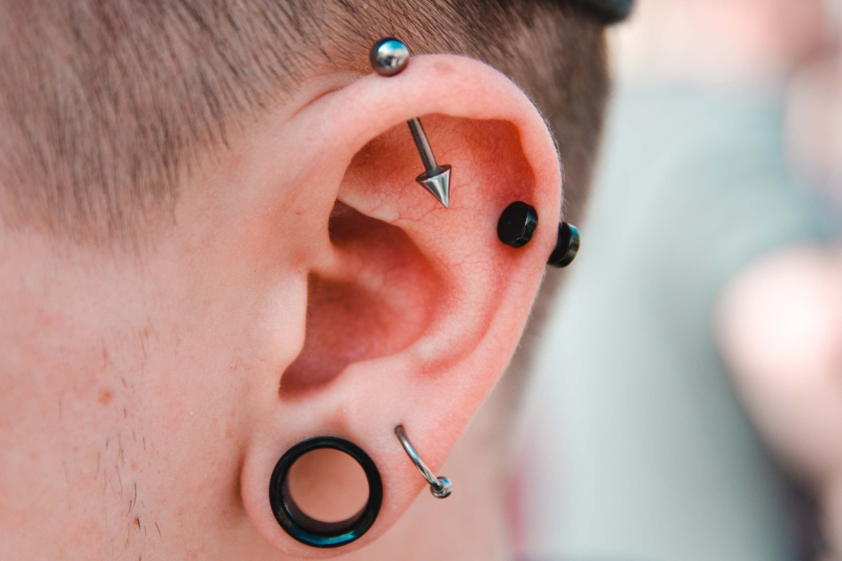 Ohr geschmückt mit einem Ohrring, zwei Piercings und einem sogenannten "Fleshtunnel"